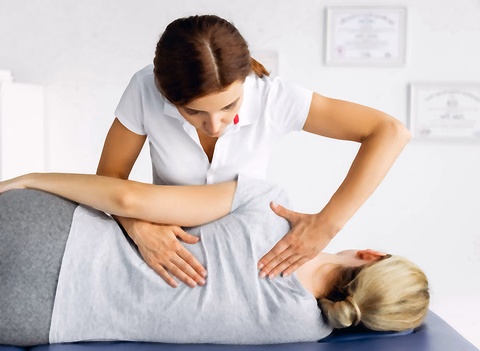 A practitioner works on a patient's lower back in a clinic room hung with framed certificates